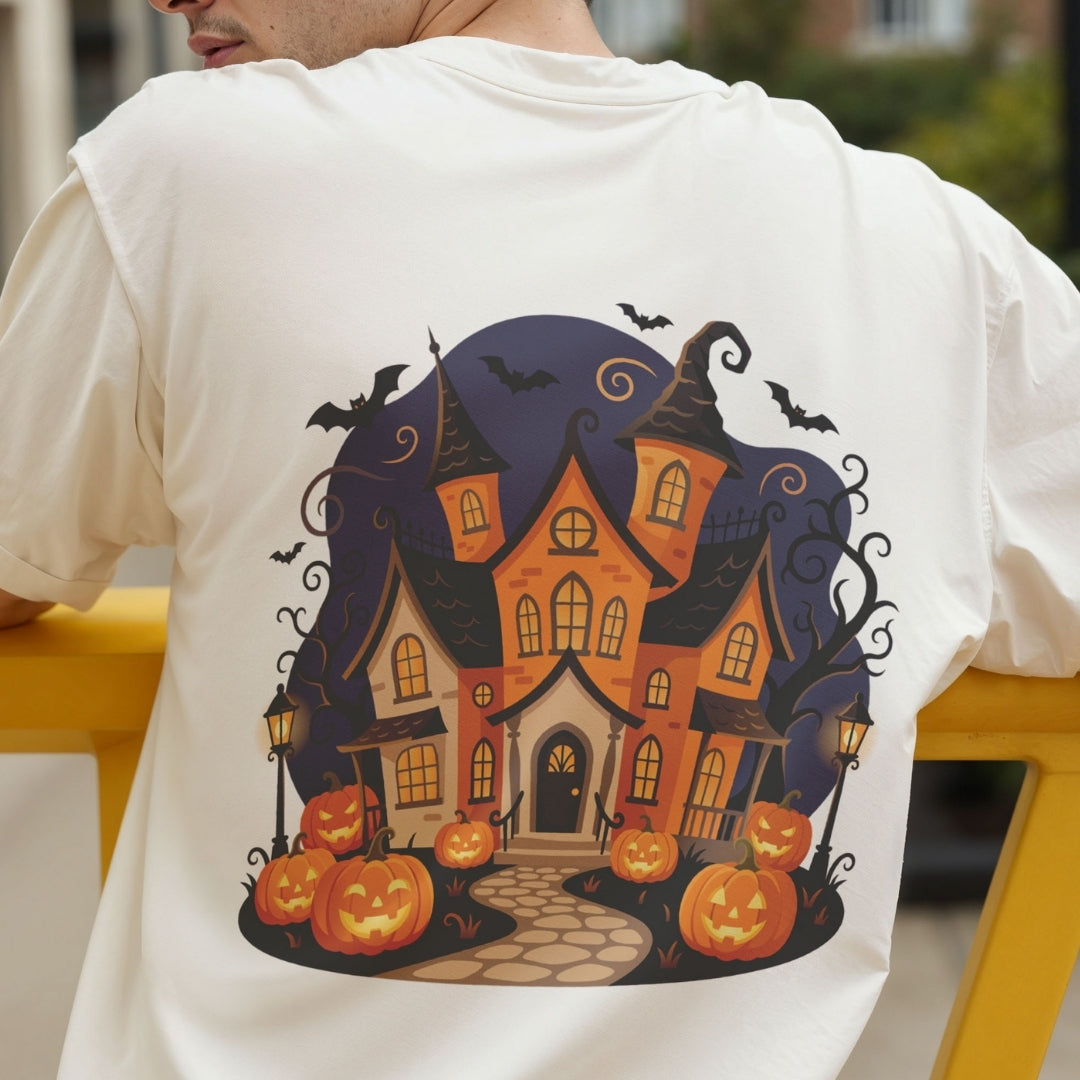 A person wearing a white T-shirt, shown from the back, featuring a large graphic print of a spooky haunted house surrounded by jack-o'-lanterns, bats, and a dark blue night sky.