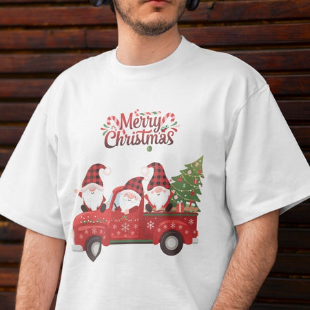 A man wearing a white crewneck t-shirt with a festive Christmas graphic. The graphic features three cartoon gnomes in a red pickup truck carrying a Christmas tree, with 'Merry Christmas' written above in a decorative red and green font.
