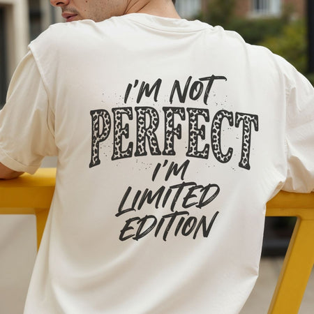 A man wearing a cream-colored t-shirt from the back, featuring a black graphic text print that reads 'I'M NOT PERFECT I'M LIMITED EDITION' with 'PERFECT' filled with a leopard print pattern.