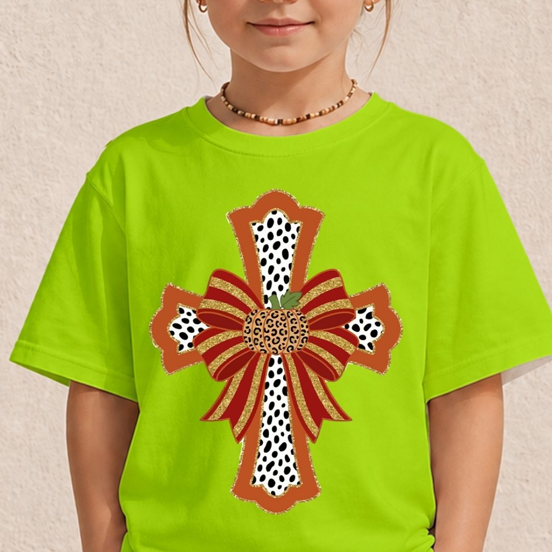 A child wearing a bright lime green t-shirt with a large decorative cross graphic on the front. The graphic features red and orange ribbon bows, leopard print details, and gold glitter accents.