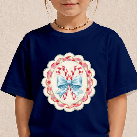 A child wearing a navy blue t-shirt with a festive Christmas graphic of candy canes and a blue bow inside a scalloped pink and white frame.