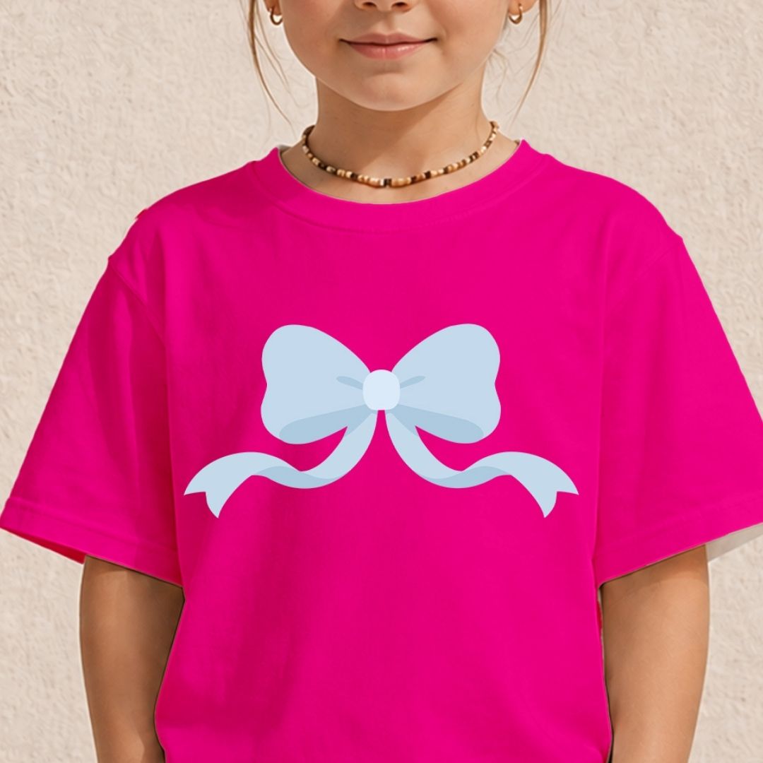 A child wearing a bright pink t-shirt with a large light blue bow graphic printed on the chest, set against a textured beige wall.