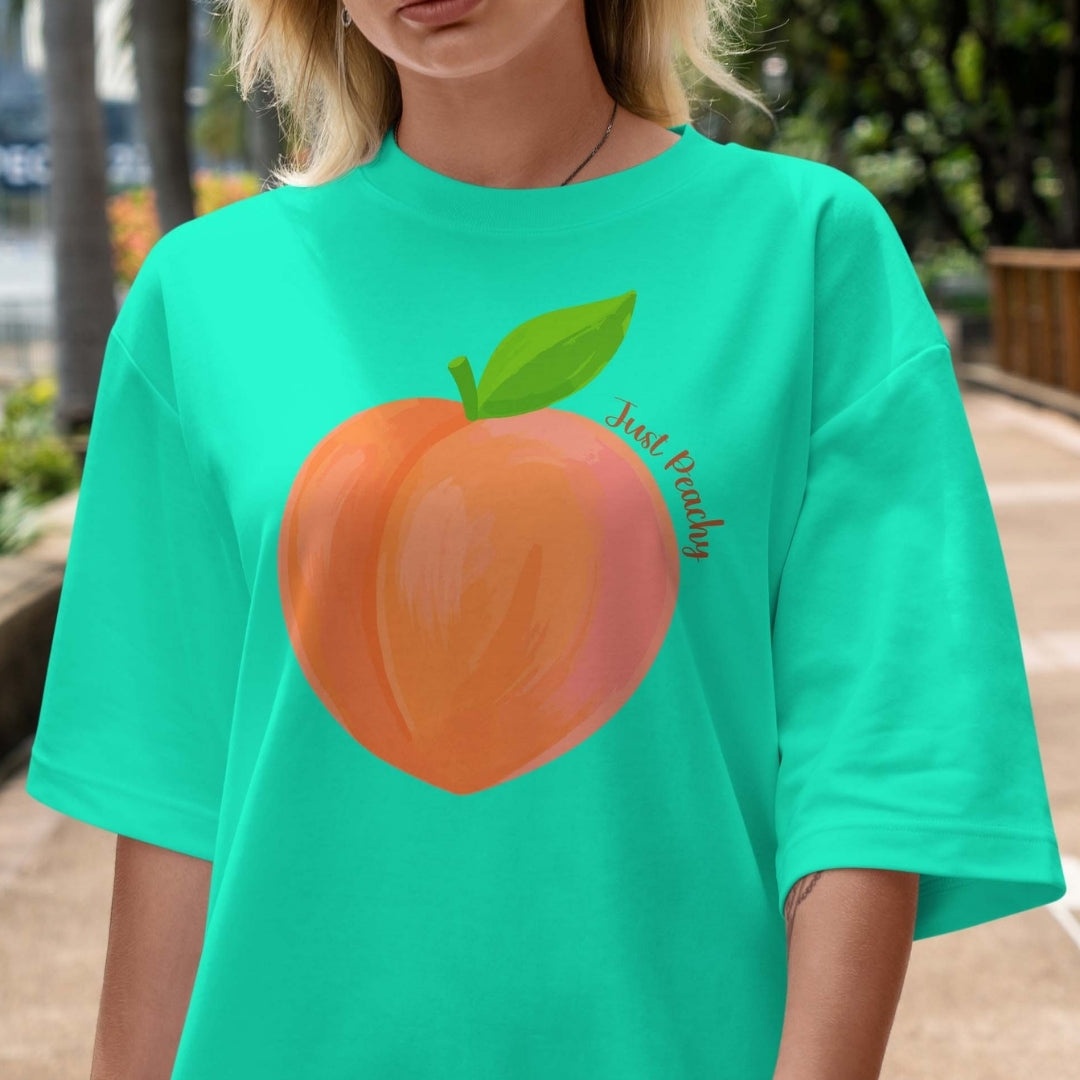 Person wearing a teal t-shirt with a peach graphic and 'Just Peachy' text.