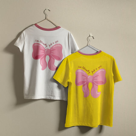 White and yellow t-shirts hanging on a wall, both showcasing the pink bow design and quote printed on the back.