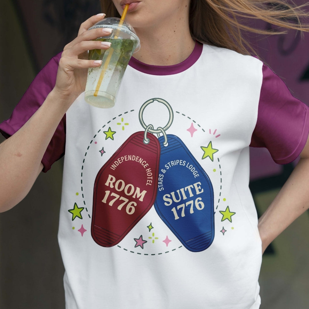 Person wearing a t-shirt with motel keychain design and holding a drink.
