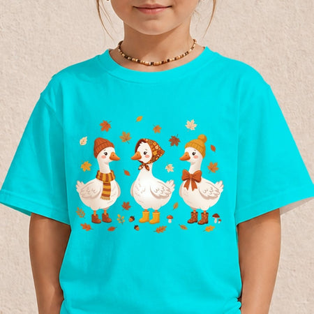 A child wearing a bright turquoise short-sleeve t-shirt with a graphic of three white geese in autumn hats and scarves, set against a light beige textured wall.