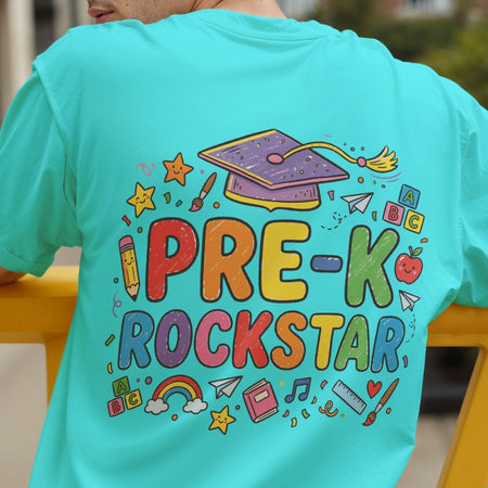 A person wearing a bright turquoise T-shirt, shown from the back. The shirt features a colorful graphic with the words 'PRE-K ROCKSTAR' in playful multicolored letters, surrounded by school-themed doodles including a purple graduation cap, stars, a pencil, an apple, and a rainbow.