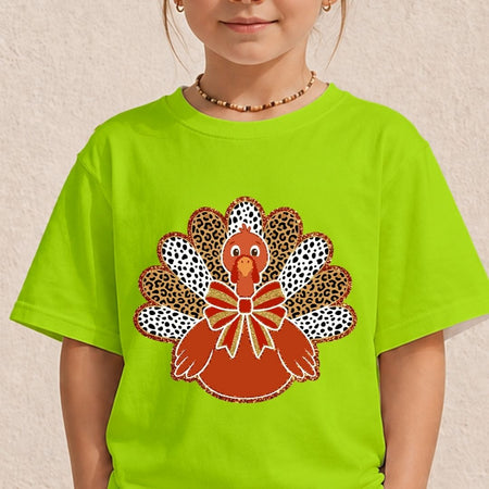 A child wearing a bright lime green t-shirt with a large embroidered turkey graphic on the front, set against a neutral textured beige wall.