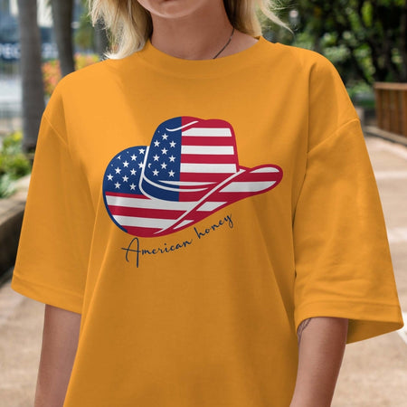 Person wearing a mustard yellow t-shirt with a graphic of a cowboy hat and American flag, text 'American honey'.