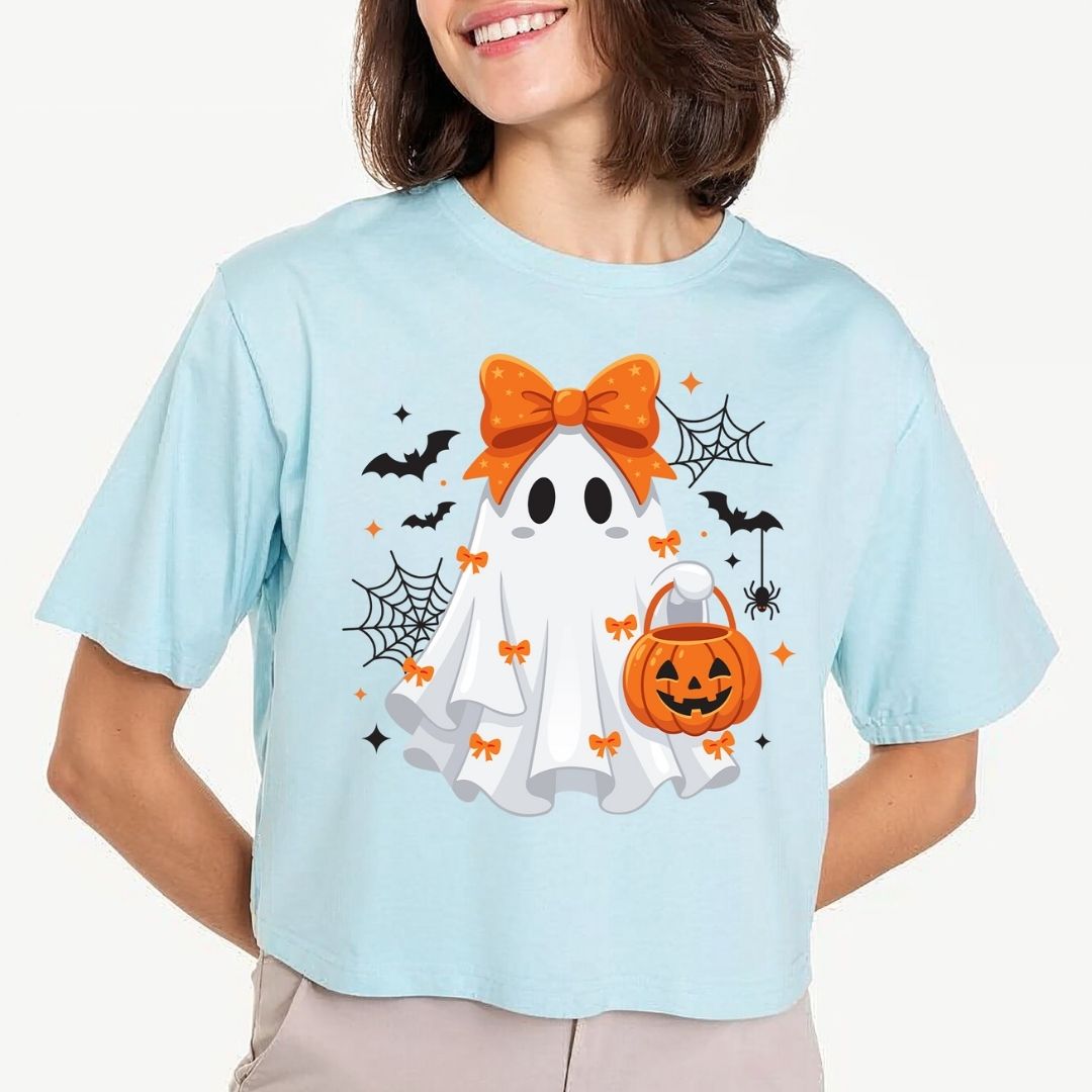 Woman wearing a light blue cropped t-shirt showcasing a playful Halloween ghost design with bats and a pumpkin basket.