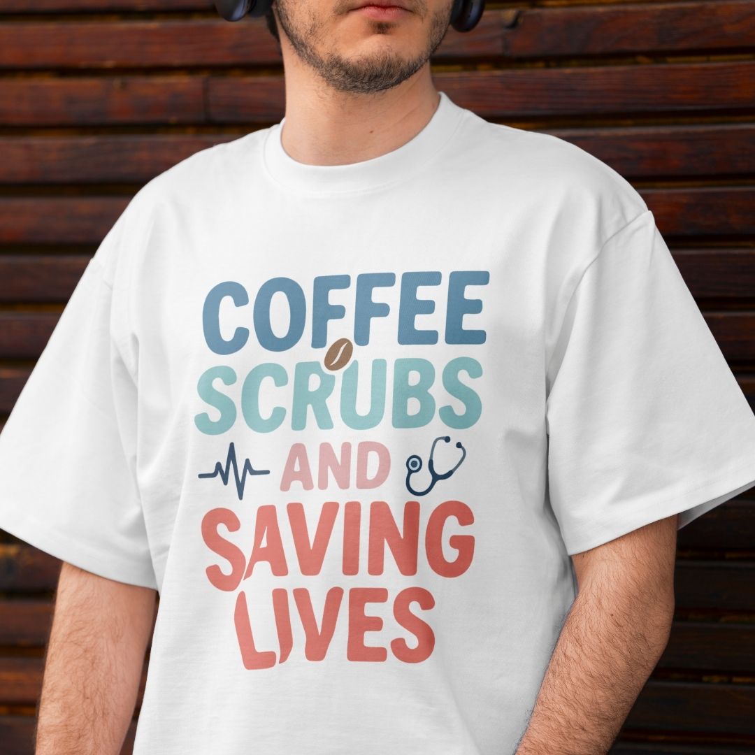 A man wearing a white graphic t-shirt with the text 'COFFEE SCRUBS AND SAVING LIVES' in blue, teal, and coral colors, set against a dark wooden background.