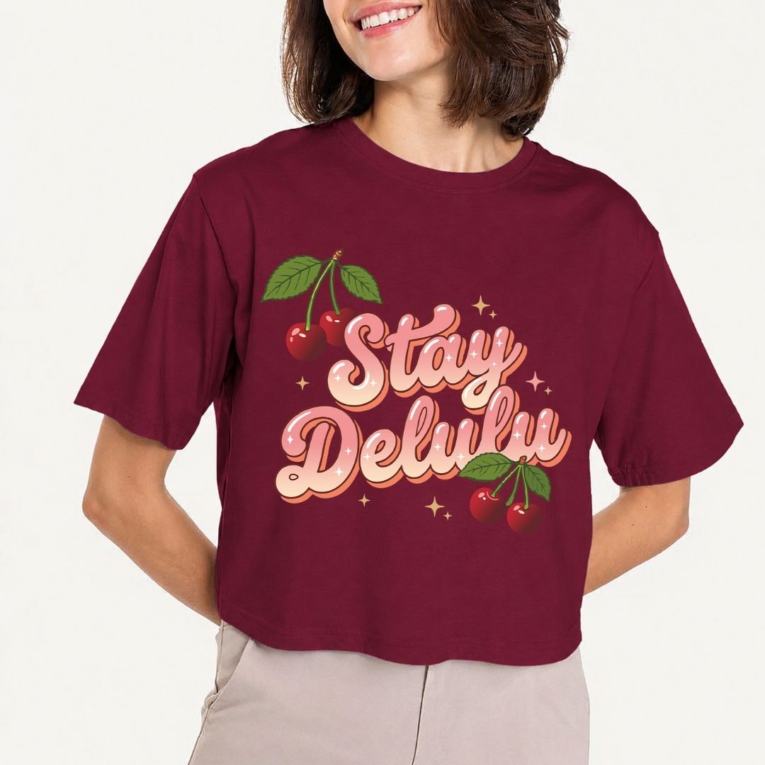 Person wearing a maroon t-shirt with 'Stay Delulw' text and cherries on a plain background