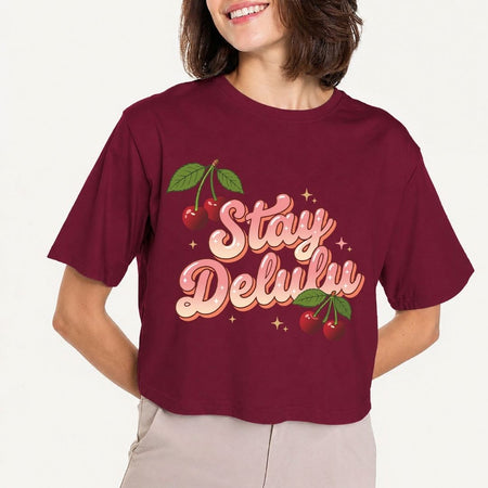 Person wearing a maroon t-shirt with 'Stay Delulw' text and cherries on a plain background