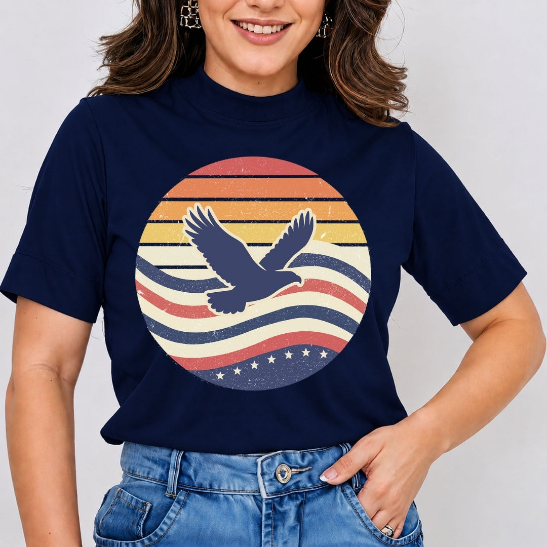 Smiling person wearing a dark blue t-shirt featuring a retro, vintage-style sunset circle with a flying eagle silhouette, wavy lines, and stars.