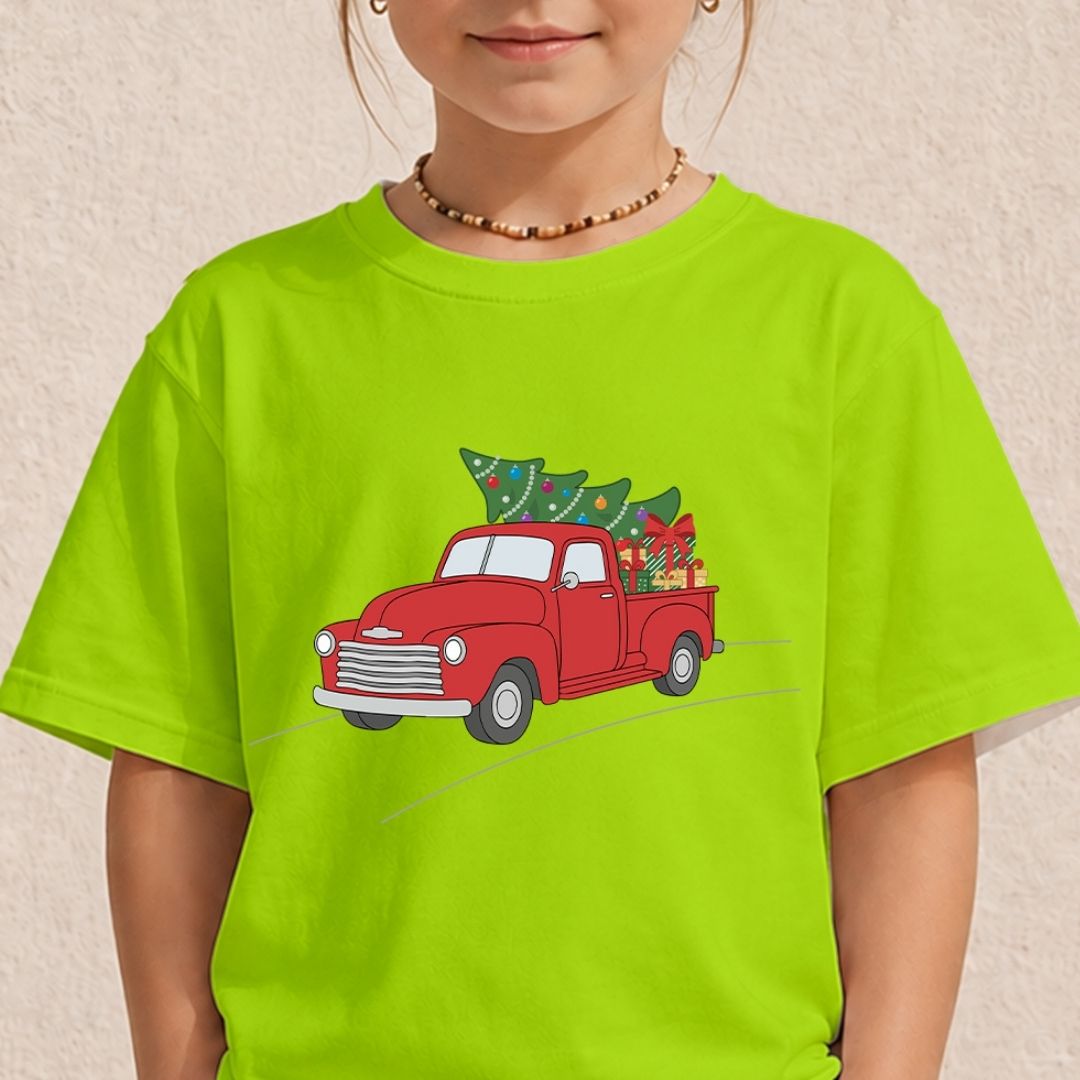 A child wearing a bright lime green t-shirt with a graphic of a red vintage truck carrying a green Christmas tree. The child is also wearing a beaded necklace against a textured beige wall.