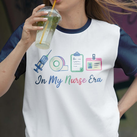 Person wearing a white t-shirt with colorful graphics and text, holding a drink.