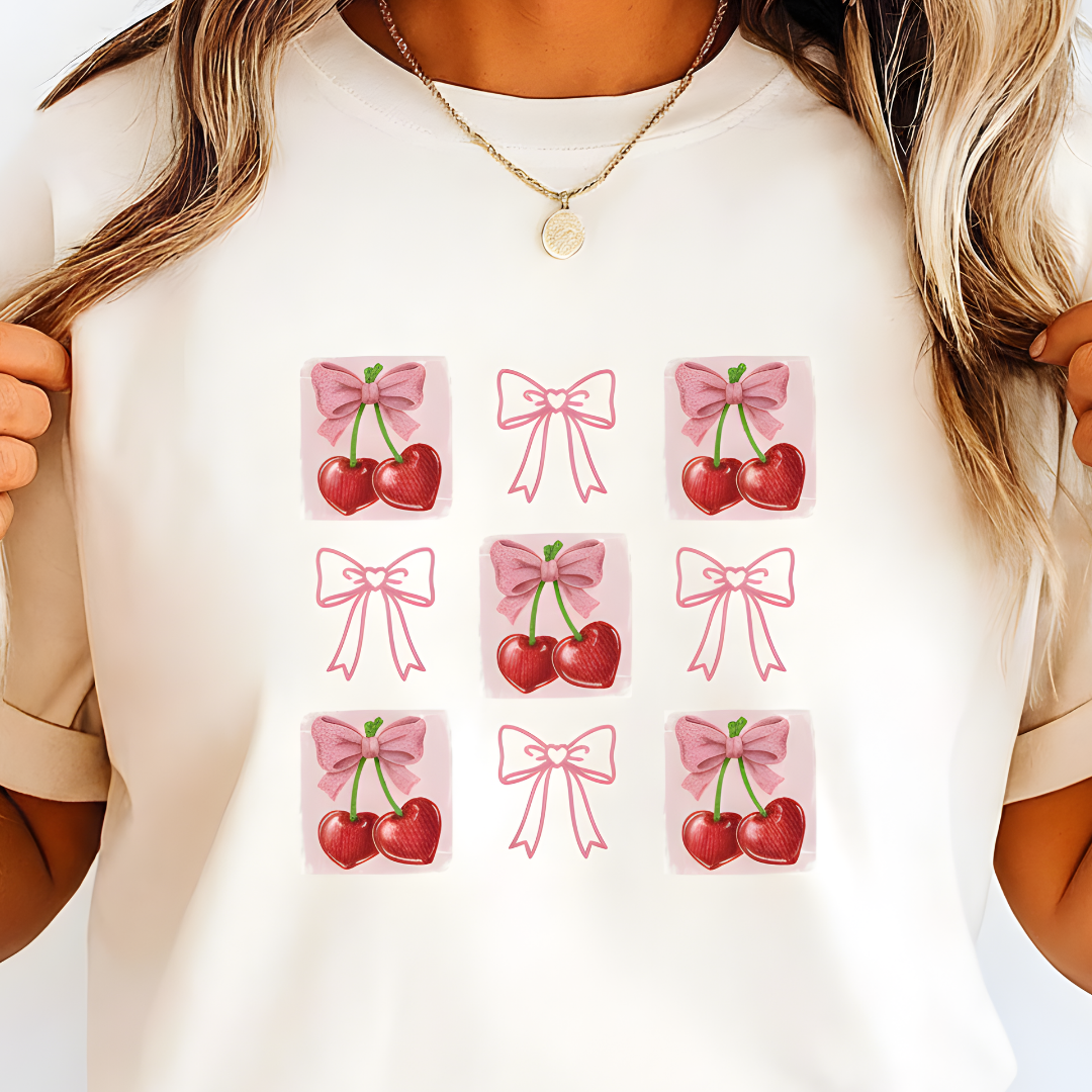 Person wearing a white t-shirt with pink bows and red cherries pattern.