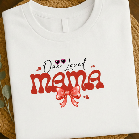 White t-shirt with 'One Loved Mama' text and red bow design on a woven surface.