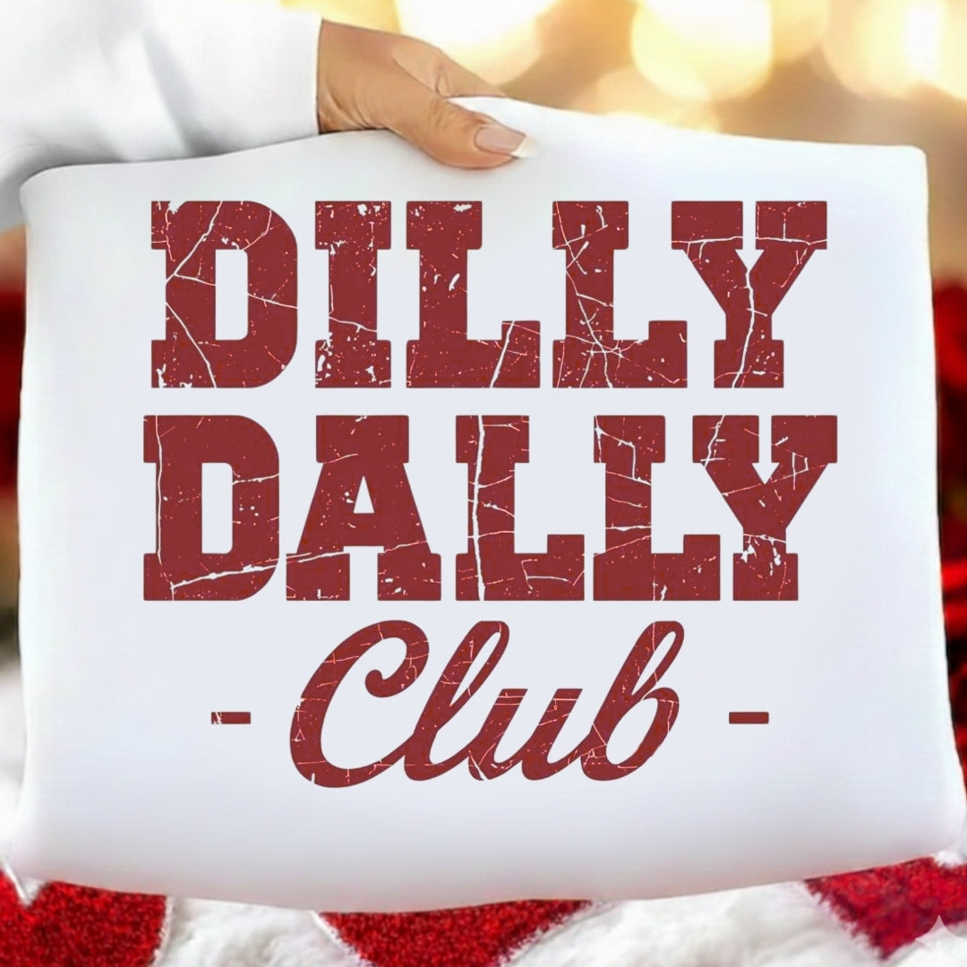 White pillow with red text 'Dilly Dally Club' held by a hand against a blurred background.