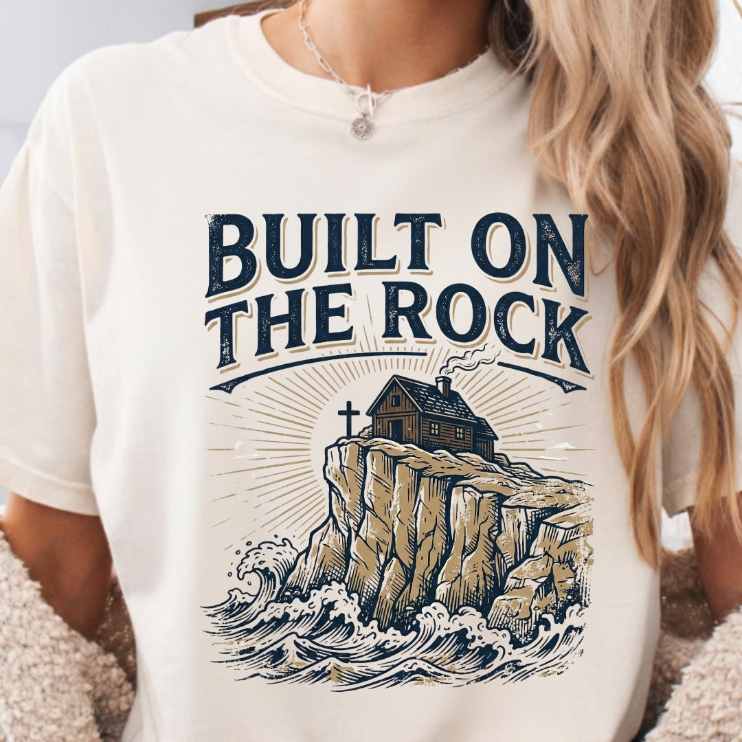 White t-shirt with 'Built on the Rock' graphic design featuring a house on a cliff.