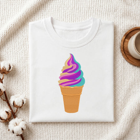 A folded white T-shirt with a colorful ice cream cone graphic, styled on a textured cream fabric with cotton bolls and a wooden cup edge visible.