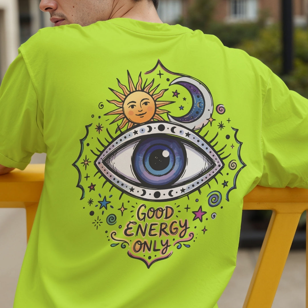 A person wearing a bright neon yellow-green t-shirt, showing the back of the shirt with a large graphic of an all-seeing eye, a smiling sun, a crescent moon, and the text 'GOOD ENERGY ONLY'.