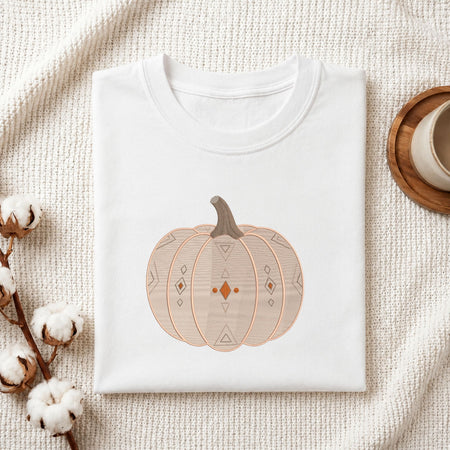 Folded white cotton t-shirt mockup featuring a geometric pumpkin machine embroidery design, styled with cotton stems and a wooden cup.   
