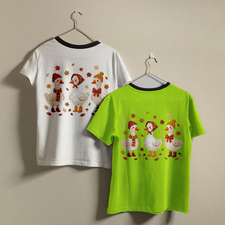 Two short-sleeve ringer T-shirts hanging on hangers against a plain beige wall. The left shirt is white with a black collar trim and shows a back graphic of three cartoon ducks wearing winter hats and scarves with autumn leaves.