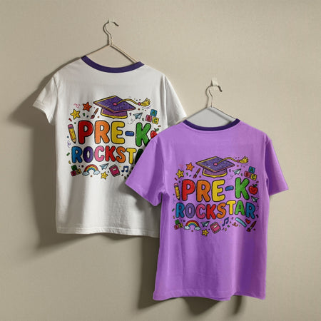 Two ringer t-shirts with purple neck and hem trims hanging on hangers against a beige wall. The left shirt is white with a colorful 'I PRE-K ROCKSTAR' graduation graphic on the back.