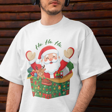 A man wearing a white crewneck t-shirt with a colorful graphic of Santa Claus popping out of a gift box with the text 'Ho Ho Ho' above him, set against a dark wooden plank background.