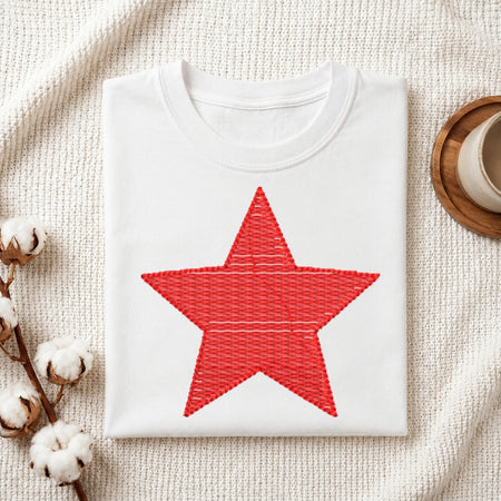 The "Be Kind" machine embroidery design stitched onto a white t-shirt, displayed on a textured white fabric background with cotton sprigs.
