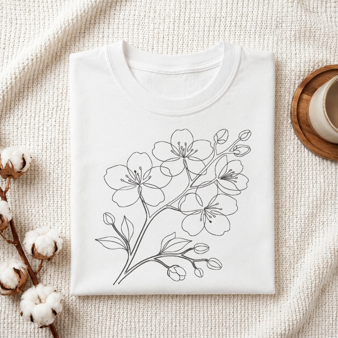 A minimalist single line art cherry blossom flower branch embroidery design stitched on the front of a folded white cotton t-shirt.