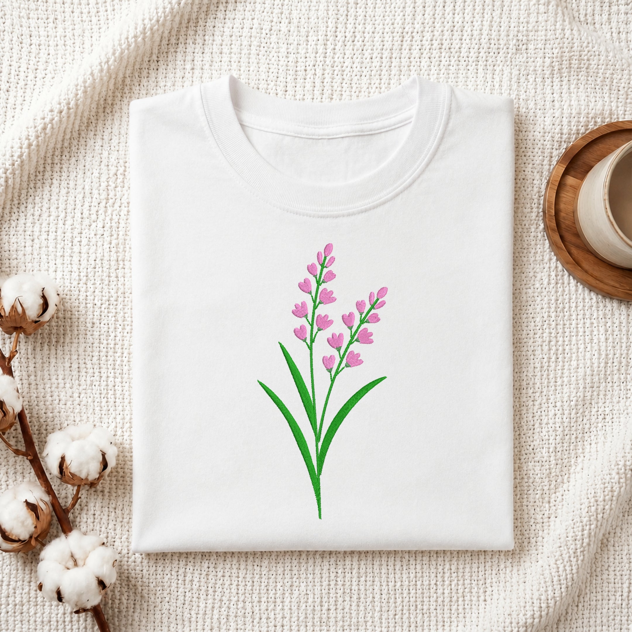 Folded white t-shirt featuring a pink lavender floral embroidery design centered on the chest.