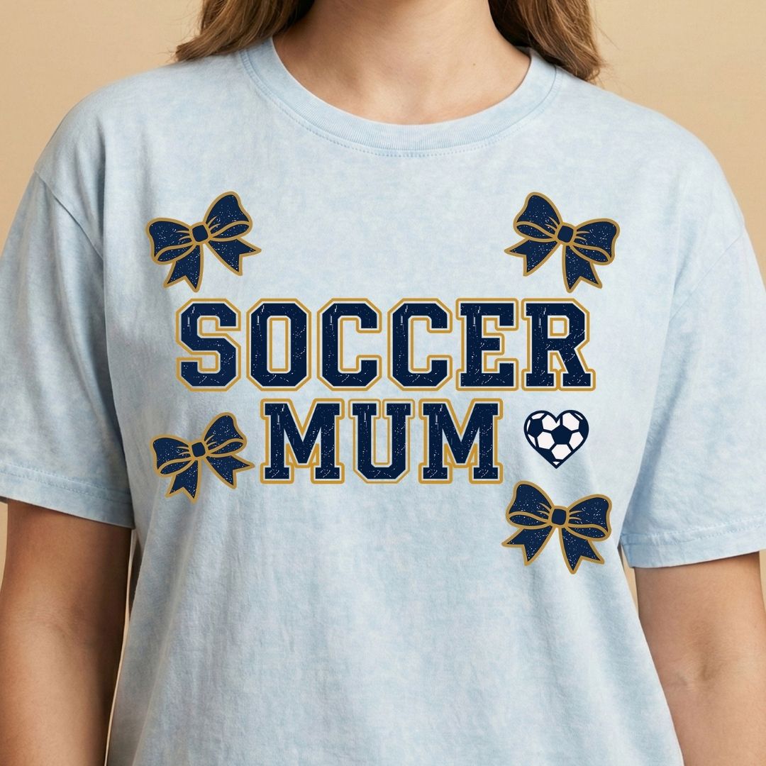 Light blue t-shirt with 'Soccer Mum' text and decorative elements on a beige background