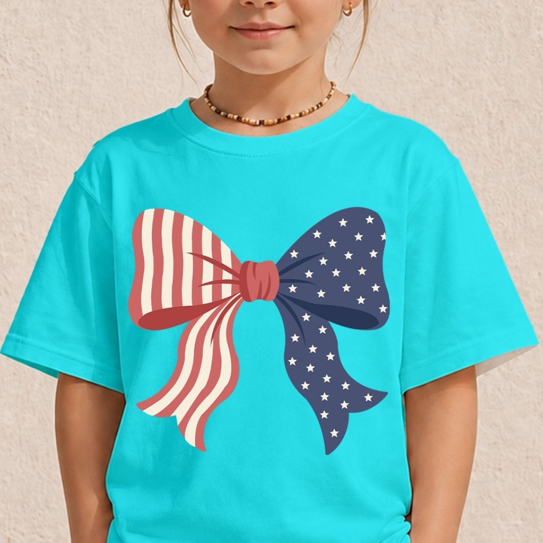 A young child wearing a bright cyan turquoise t-shirt displaying a large patriotic red, white, and blue coquette bow graphic on the front.