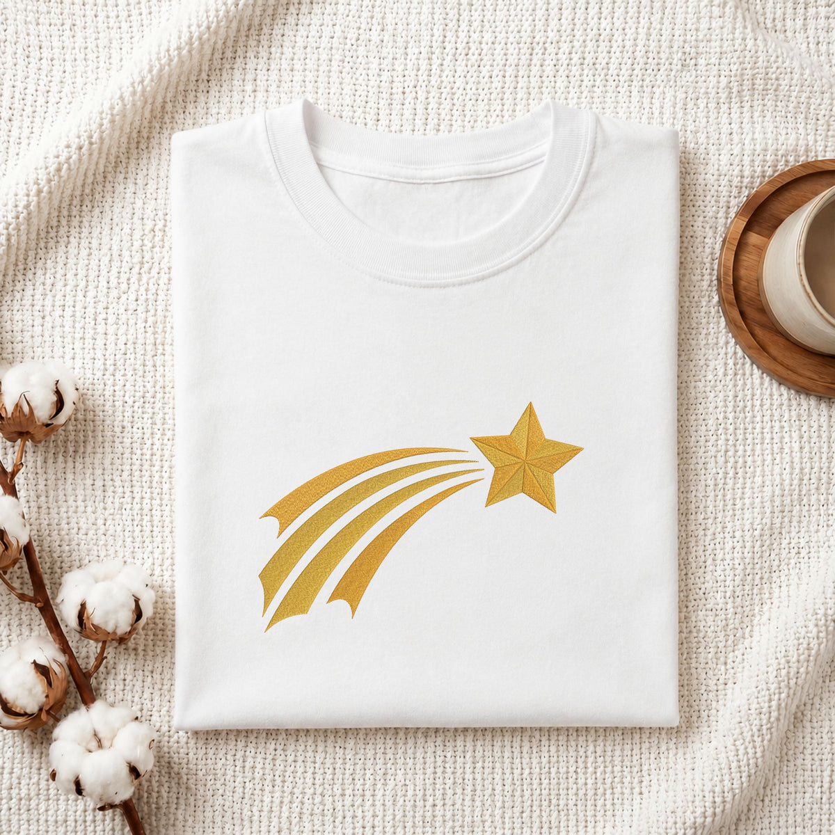  Folded white cotton t-shirt mockup featuring a golden shooting star machine embroidery design, styled with cotton stems and a wooden cup   
