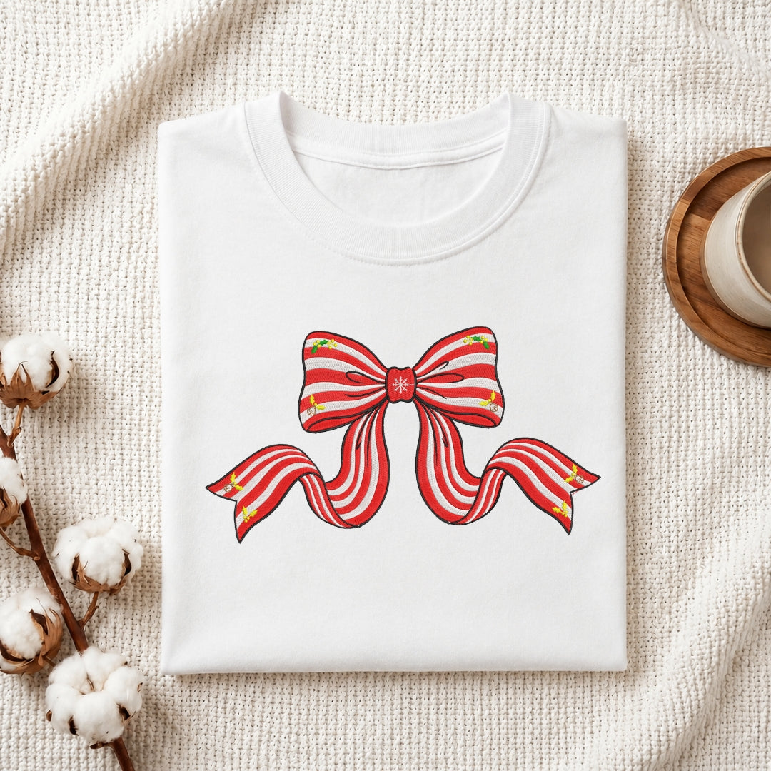 A white t-shirt featuring an embroidered design of a red and white striped holiday ribbon bow with small holly accents.