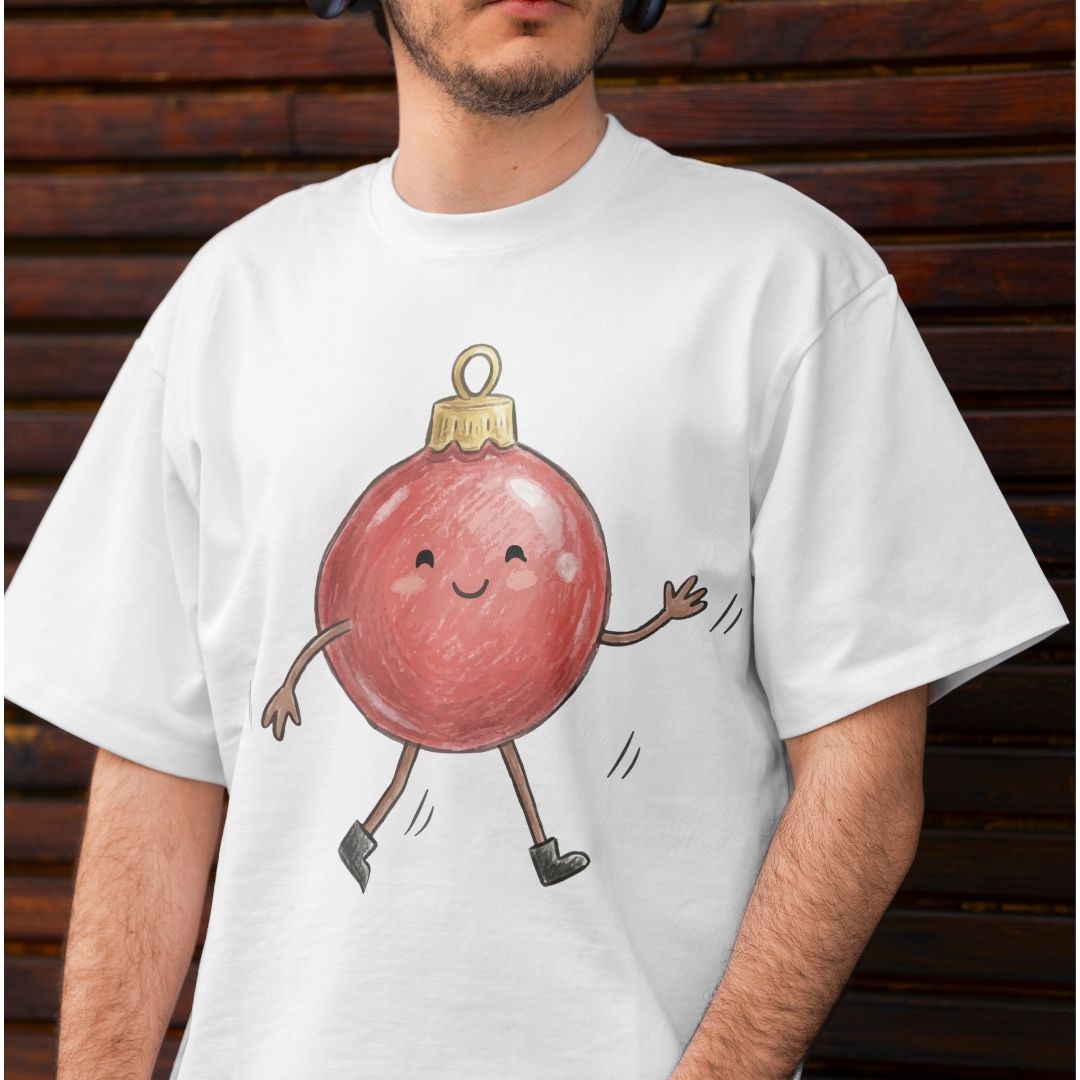 A man wearing a white crewneck t-shirt with a graphic of a cute, smiling red Christmas ornament character with legs and arms, posed against a dark brown wooden background.