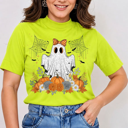 A woman wearing a bright lime green mock-neck t-shirt with a Halloween graphic of a ghost, pumpkins, spiders, and bats, paired with blue jeans.