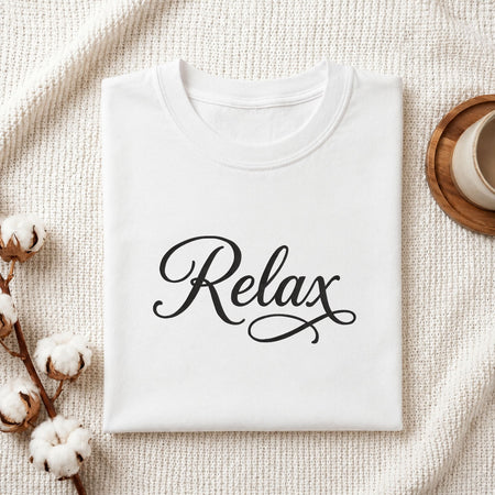 Folded white cotton t-shirt mockup featuring a "Relax" script machine embroidery design, styled with cotton stems and a wooden cup