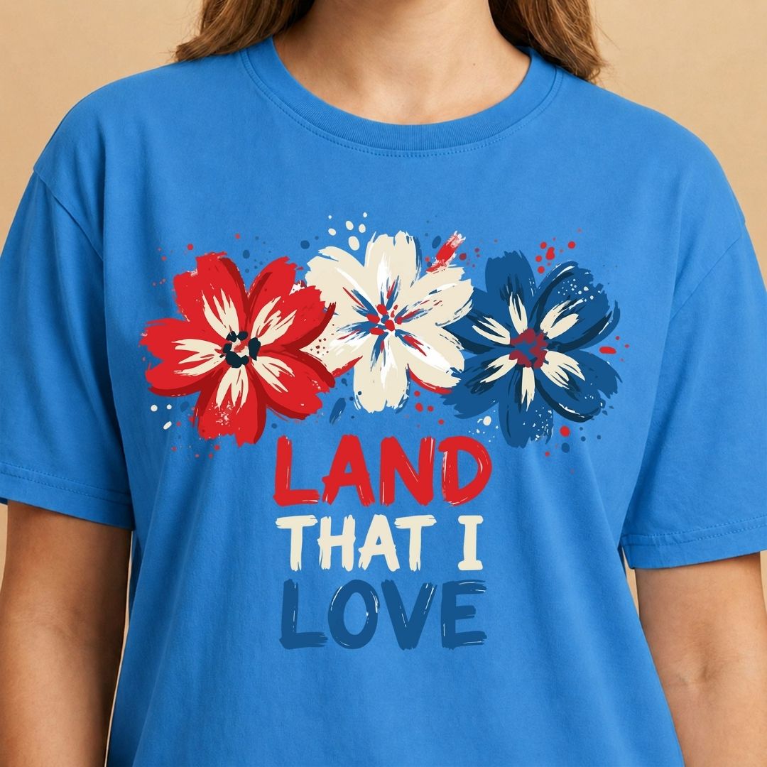 Blue t-shirt with red, white, and blue flowers and 'LAND THAT I LOVE' text on a beige background