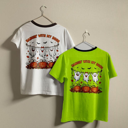 Two children's short-sleeve ringer T-shirts hanging on hangers against a plain beige wall. The left shirt is white with a dark brown collar and features a Halloween graphic with ghosts, pumpkins, bats, and the text 'HARSHIN' WITH MY BOOS' on the back.