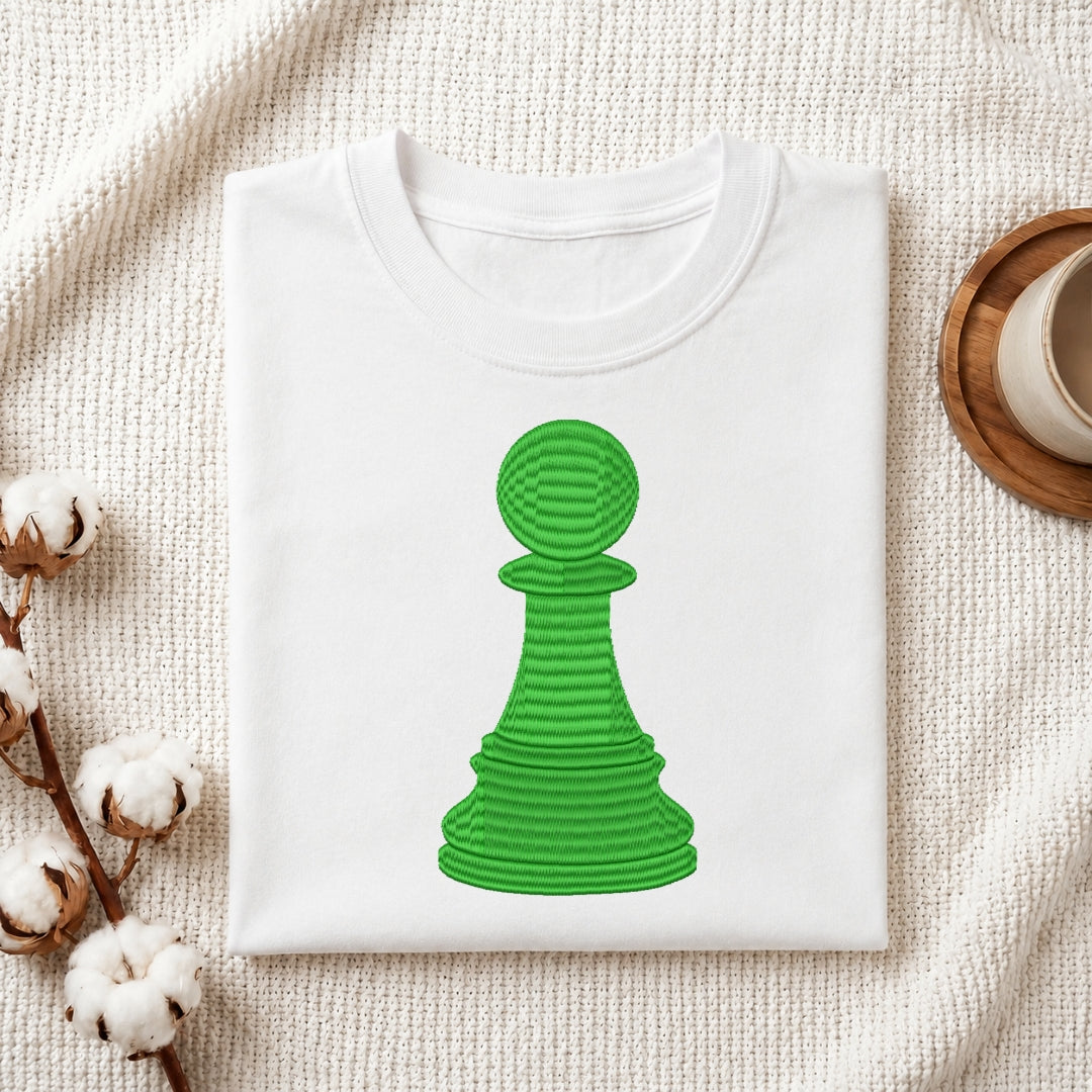 A folded white t-shirt featuring the embroidered green chess pawn design centered on the fabric.