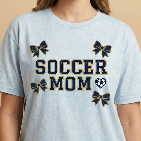 Light blue t-shirt with 'Soccer Mom' text and decorative elements on a beige background