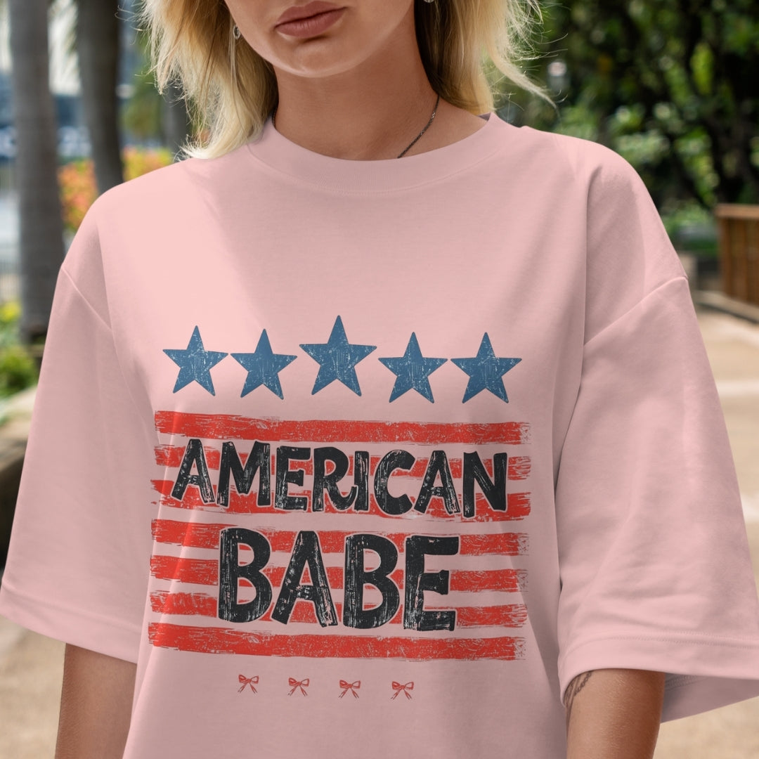 Person wearing a pink t-shirt with 'American Babe' print outdoors.