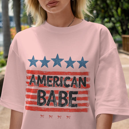 Person wearing a pink t-shirt with 'American Babe' print outdoors.