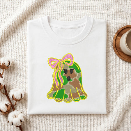 Folded white cotton t-shirt mockup featuring a cute camo ghost machine embroidery design, styled with cotton stems and a wooden cup   