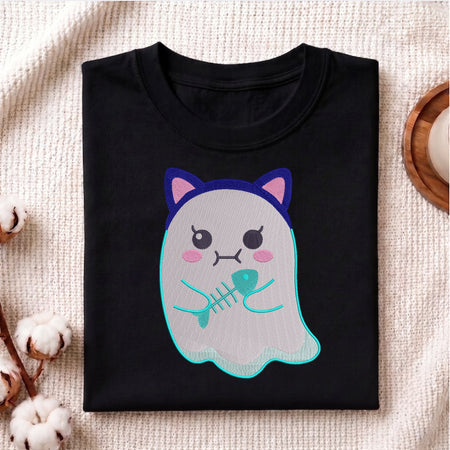 A folded black t-shirt with a cute cartoon ghost graphic holding a fish skeleton, displayed on a textured beige fabric background with decorative cotton bolls.
