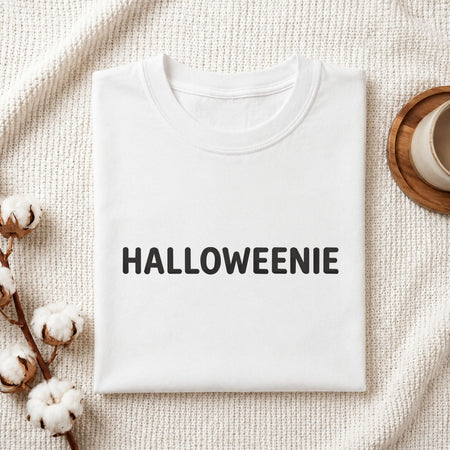 Folded white cotton t-shirt mockup featuring a "HALLOWEENIE" machine embroidery design, styled with cotton stems and a wooden cup