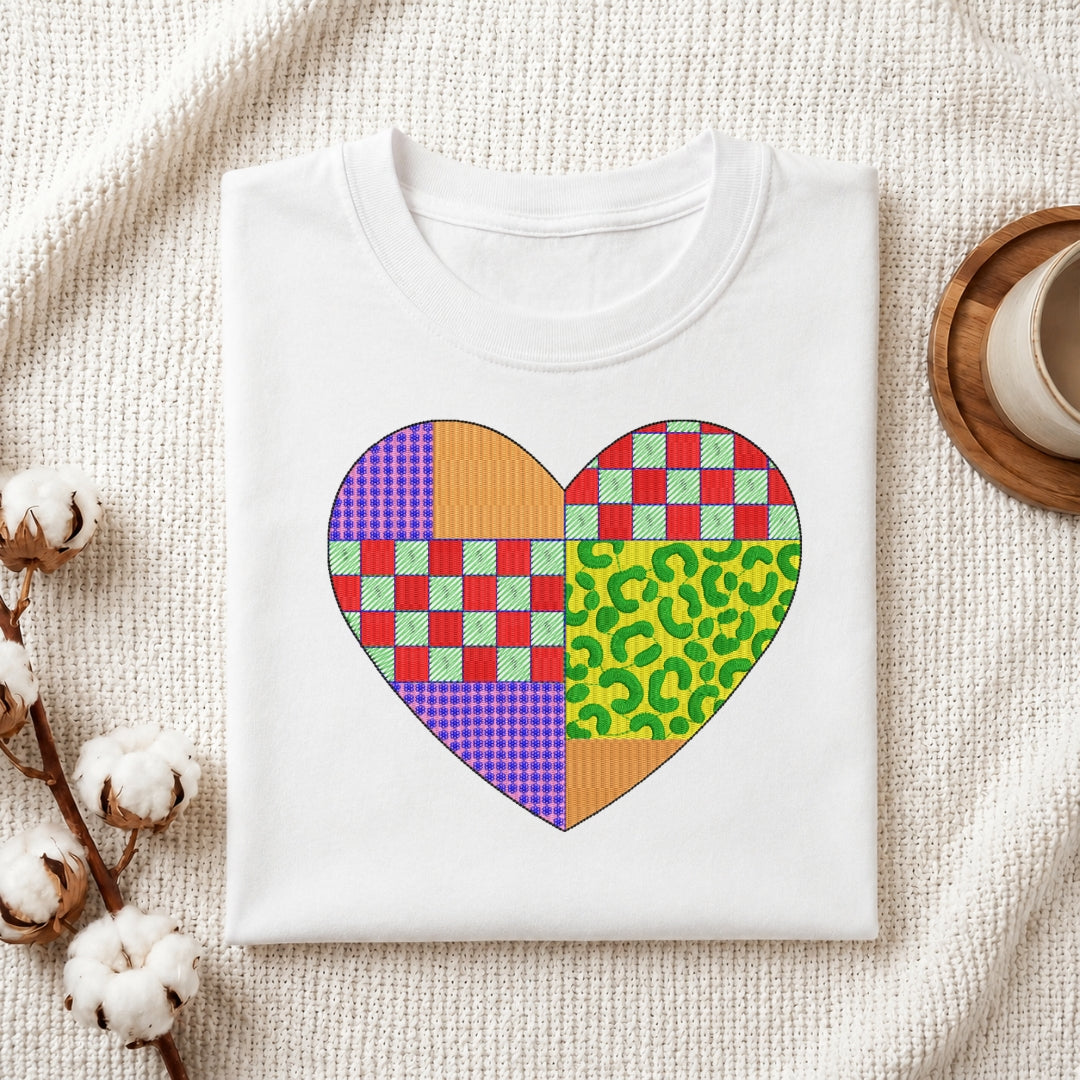 A colorful heart embroidery design featuring patchwork patterns displayed within a wooden hoop on white fabric, with thread spools nearby.